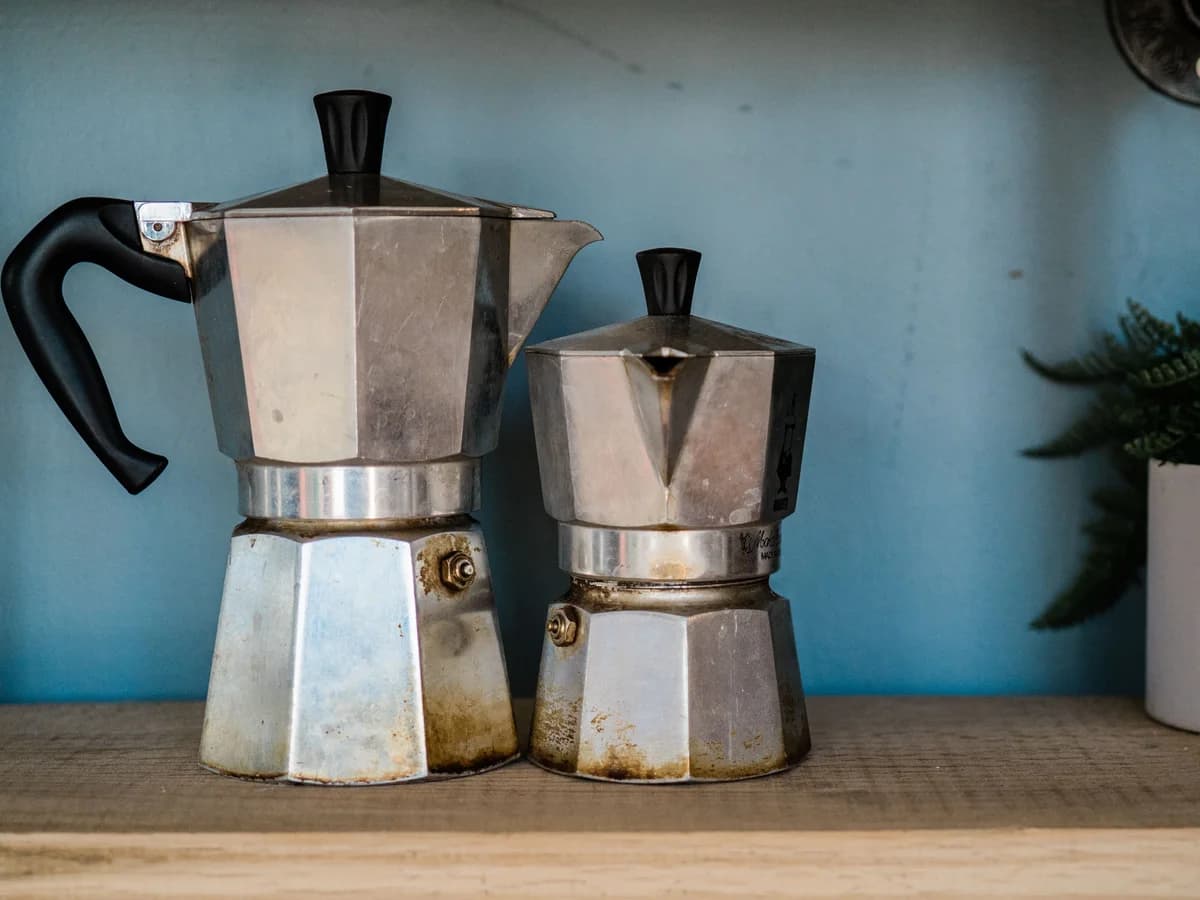 Two aluminium moka pots side by side on a wooden shelf, showing their octagonal bases and black handles.
