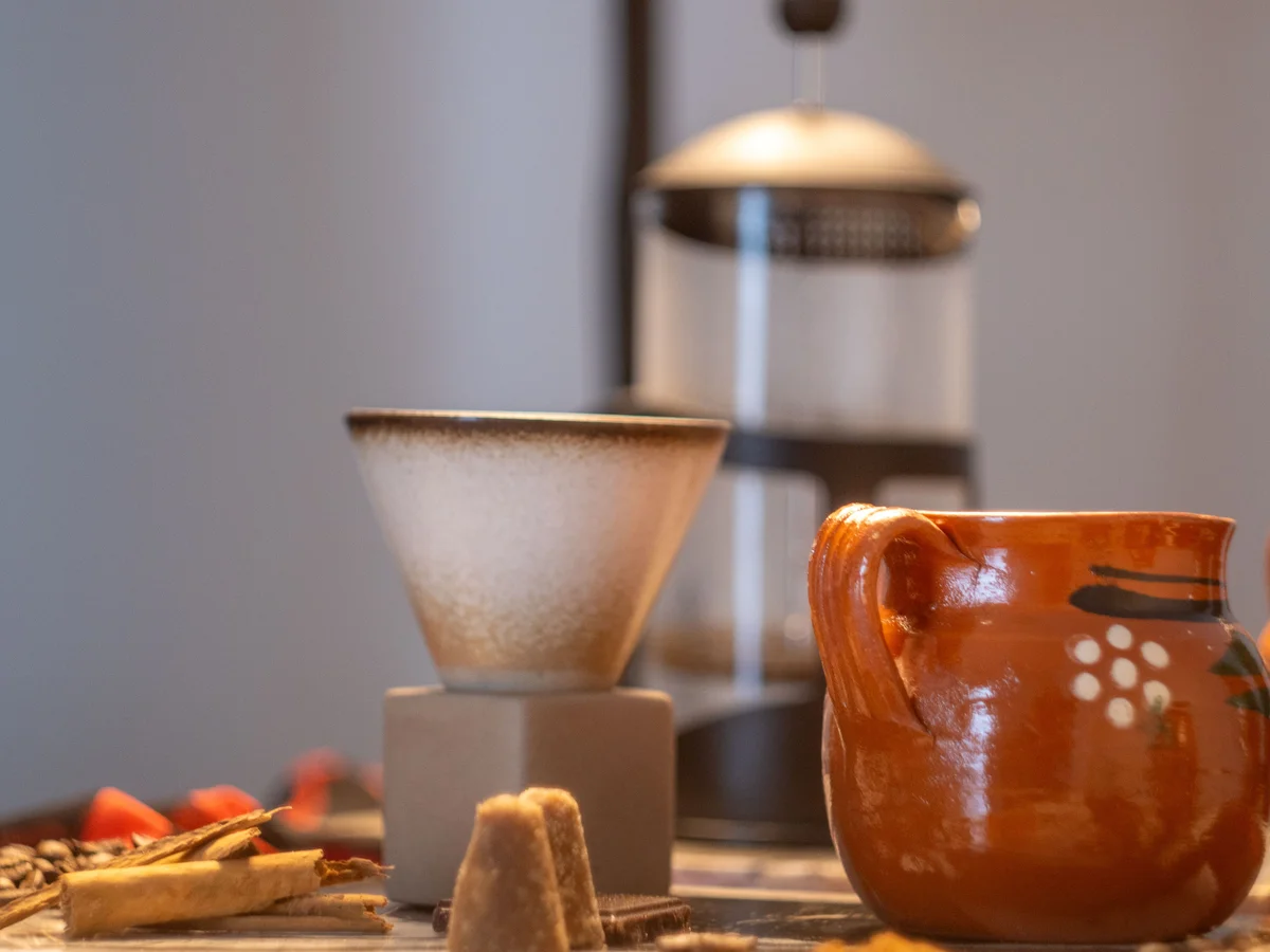 A glazed earthenware jug beside cinnamon sticks and cones of unrefined piloncillo sugar.
