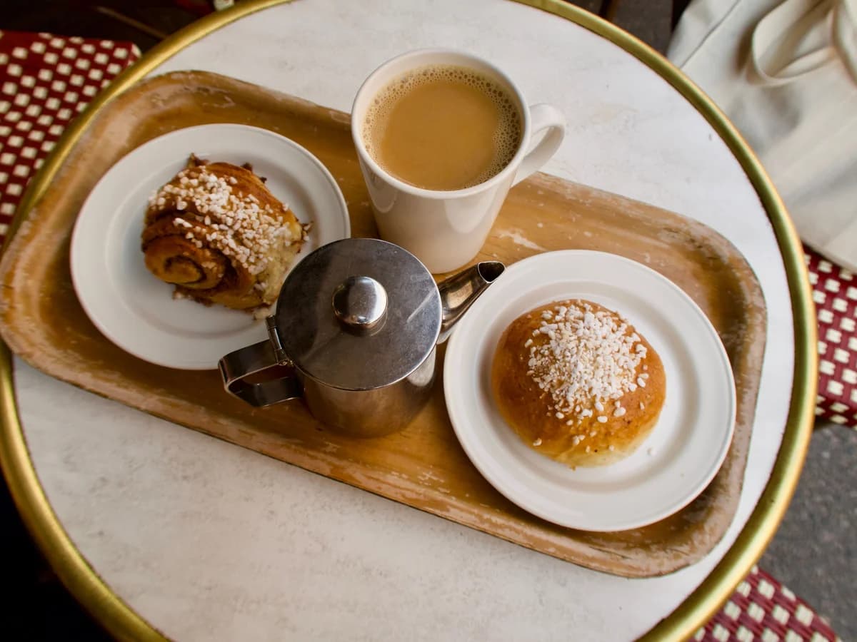 A tray holding a mug of milky coffee, a cinnamon bun and a pearl-sugar bun on small plates.