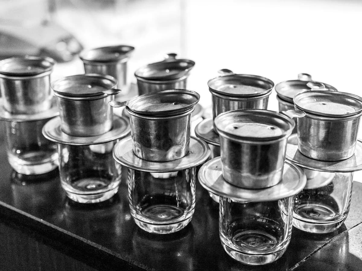Rows of stainless steel phin filters resting on glasses, ready for brewing.